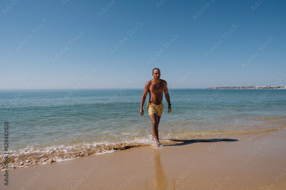 BOY COMING OUT OF THE SEA ON HIS VACATION AND WALKING ON THE BEACH