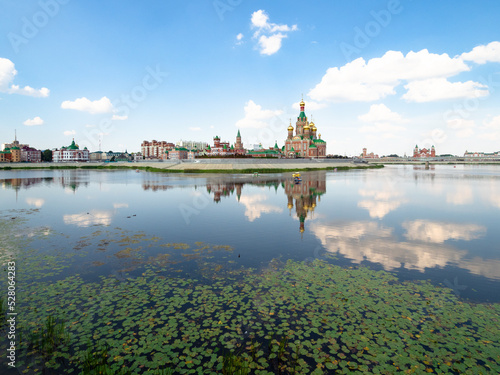 surface Malaya Kokshaga river overgrown with green water lily leaves and view of Voskresenskaya embankment with Cathedral of the Annunciation of the Blessed Virgin Mary in Yoshkar-ola city in summer
