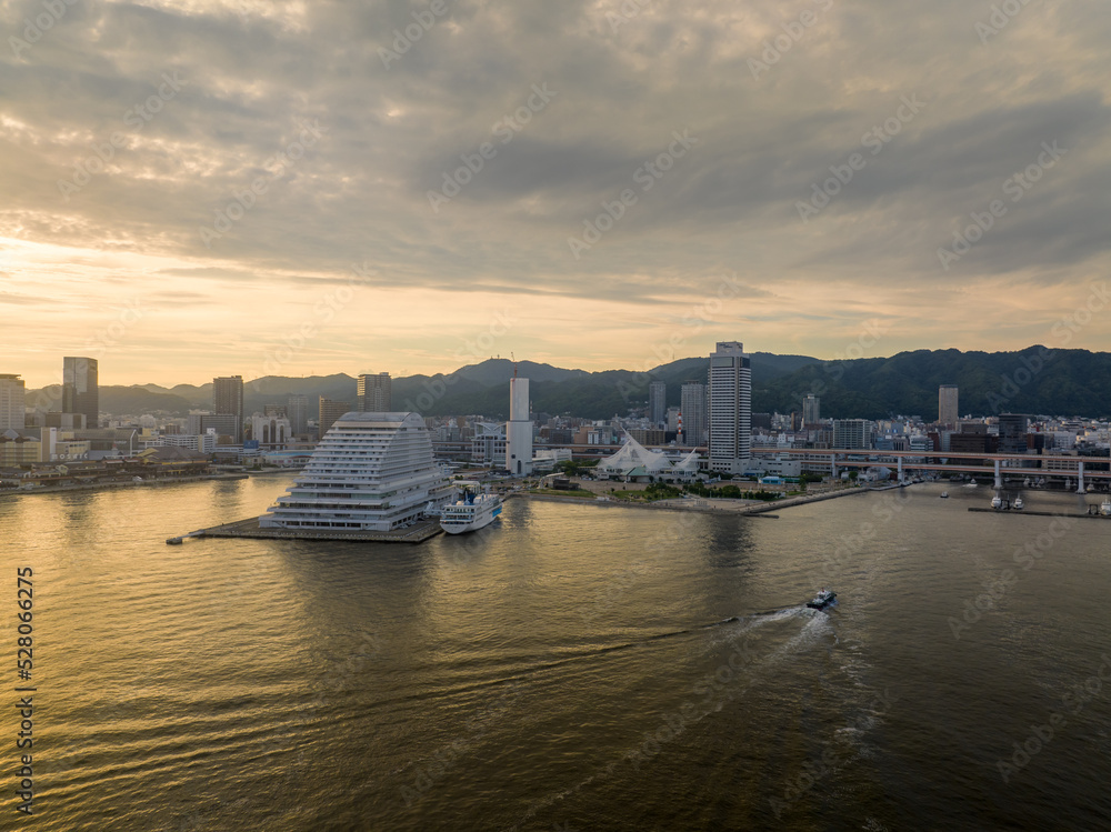 Naklejka premium Small boat passes luxury cruise ship docked at waterfront hotel as sun sets