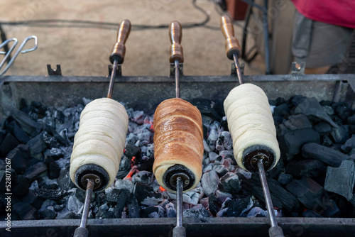 Delicious kurtos being prepared on a slow fire. Close-up image of three Hungarian buns being prepared on metal rods over the glowing charcoal. One of them is almost ready to be tasted. photo