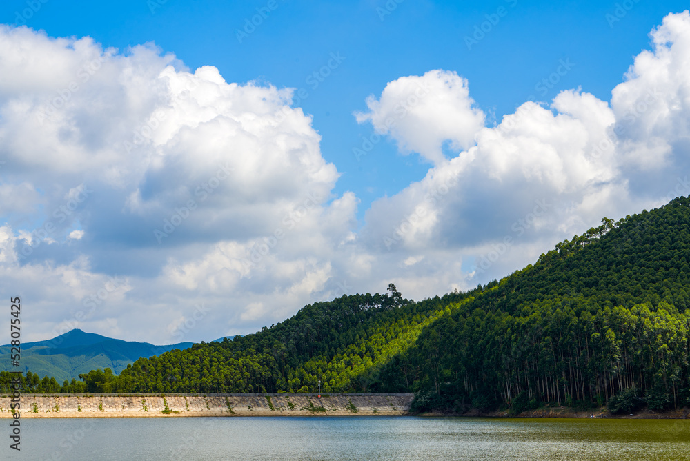 View of blue sky, white clouds and green hills and forest at outdoor reservoir
