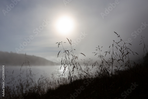 Hay in the foreground, silhouette image. In the background is the river Teno in Finnish Lapland. Foggy, early morning. The atmosphere is slow and calm, the sun has just risen.