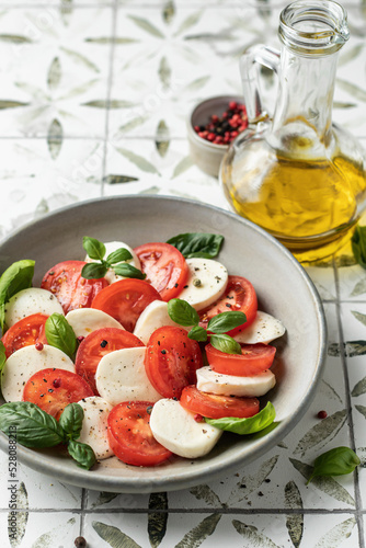 Plate of delicious Caprese Salad with Mozzarella Cheese, Tomatoes and Basil on printed tile background