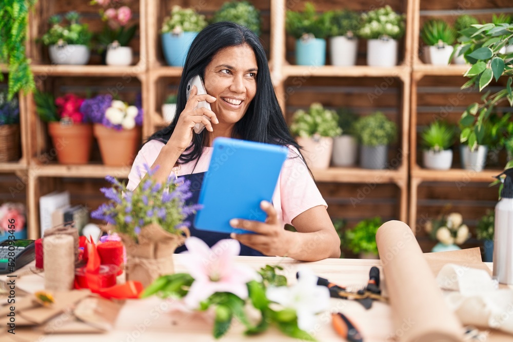 Middle age hispanic woman florist talking on smartphone using touchpad at florist Middle age hispanic woman florist talking on smartphone using touchpad at florist