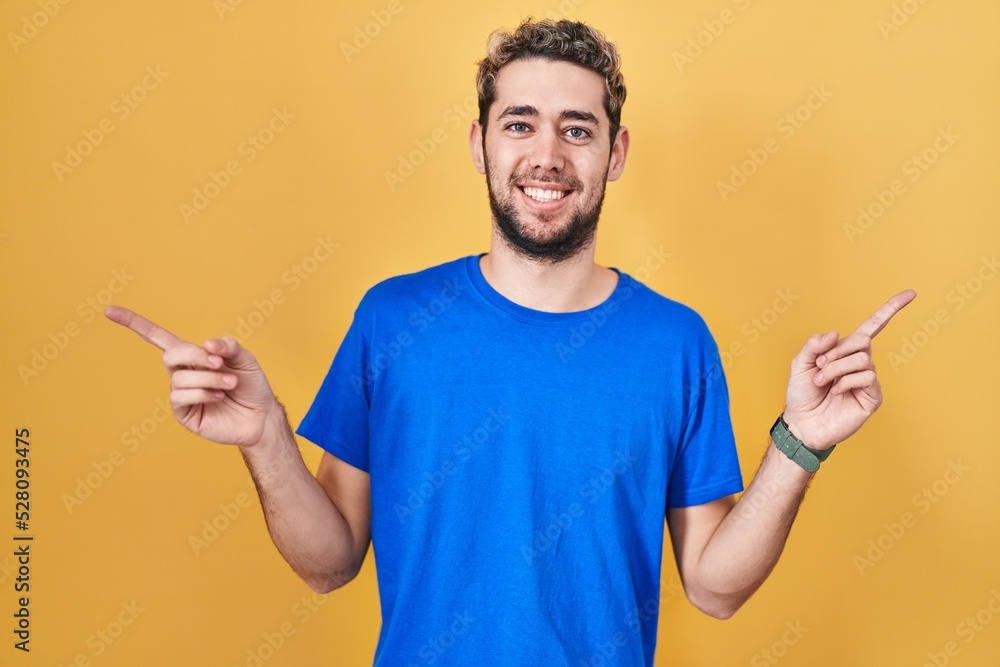 Hispanic man with beard standing over yellow background smiling confident pointing with fingers to different directions. copy space for advertisement
