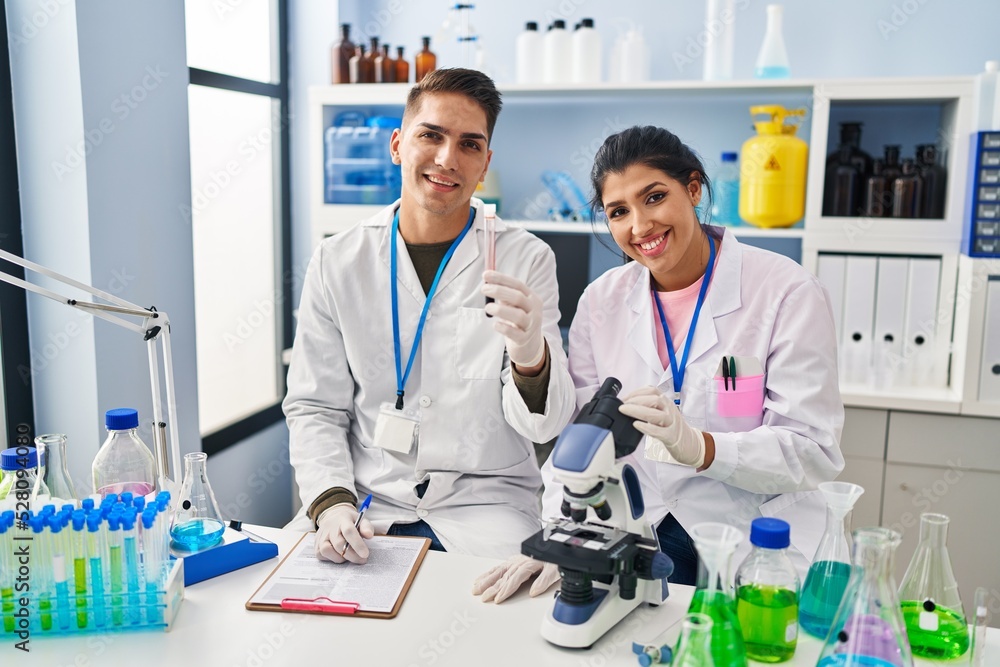 Man and woman scientists partners analysing blood test tube at laboratory Man and woman scientists partners analysing blood test tube at laboratory