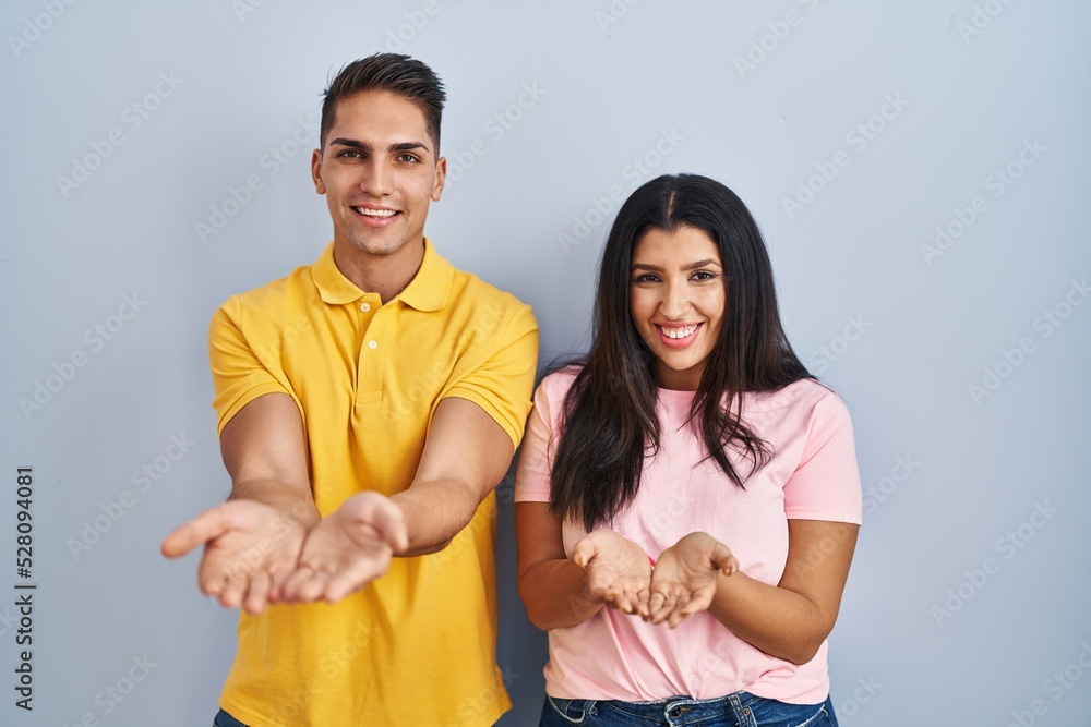 Young couple standing over isolated background smiling with hands palms together receiving or giving gesture. hold and protection Young couple standing over isolated background smiling with hands palms together receiving or giving gesture. hold and protection