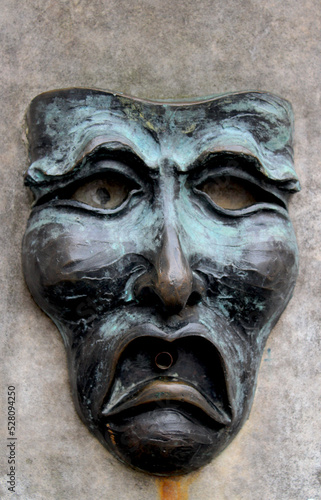 Bronze with verdigris human face, with downturned mouth, set in stone as a water fountain photo