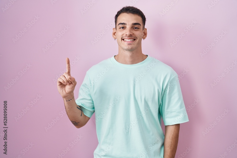 Handsome hispanic man standing over pink background showing and pointing up with finger number one while smiling confident and happy. Handsome hispanic man standing over pink background showing and pointing up with finger number one while smiling confident and happy.