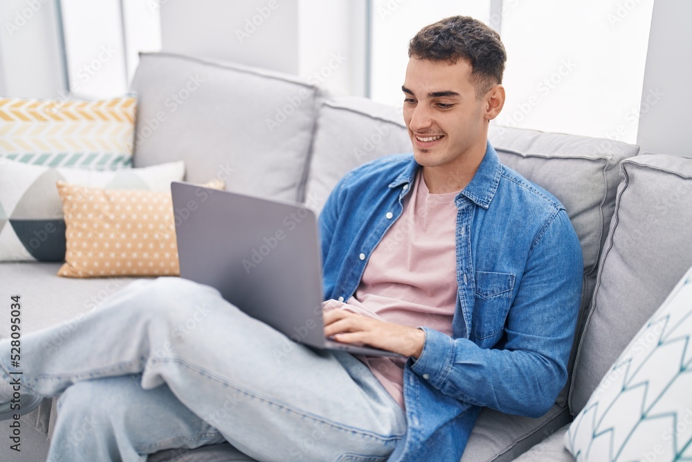 Young hispanic man using laptop sitting on sofa at home Young hispanic man using laptop sitting on sofa at home
