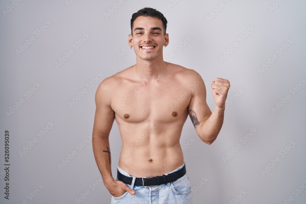 Handsome hispanic man standing shirtless very happy and excited doing winner gesture with arms raised, smiling and screaming for success. celebration concept.