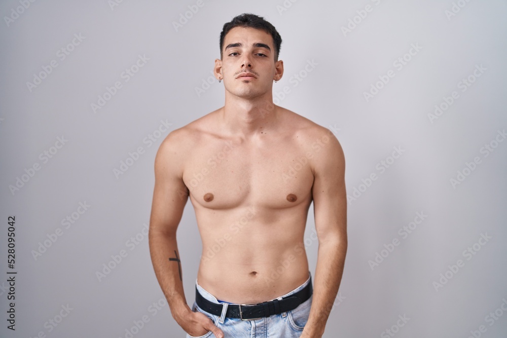 Handsome hispanic man standing shirtless looking sleepy and tired, exhausted for fatigue and hangover, lazy eyes in the morning.