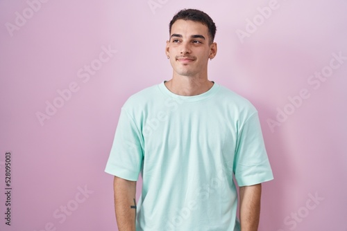 Handsome hispanic man standing over pink background smiling looking to the side and staring away thinking.