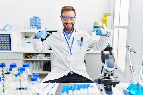 Middle age man working at scientist laboratory looking confident with smile on face  pointing oneself with fingers proud and happy.