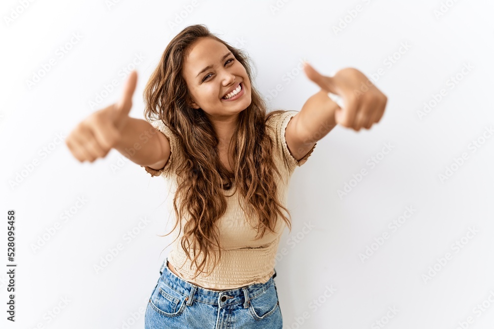 Beautiful hispanic woman standing over isolated while background approving doing positive gesture with hand, thumbs up smiling and happy for success. winner gesture. Beautiful hispanic woman standing over isolated while background approving doing positive gesture with hand, thumbs up smiling and happy for success. winner gesture.