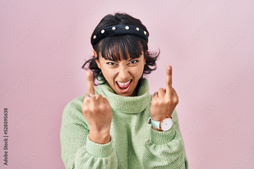 Young beautiful woman standing over pink background showing middle finger doing fuck you bad expression, provocation and rude attitude. screaming excited Young beautiful woman standing over pink background showing middle finger doing fuck you bad expression, provocation and rude attitude. screaming excited