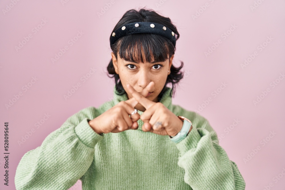 Young beautiful woman standing over pink background rejection expression crossing fingers doing negative sign Young beautiful woman standing over pink background rejection expression crossing fingers doing negative sign