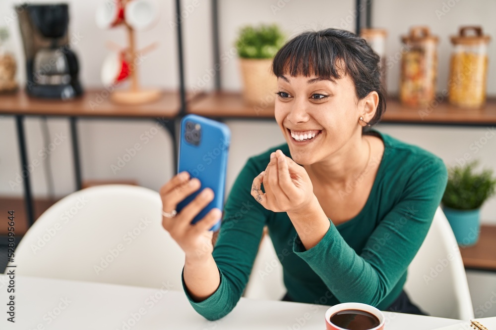 Young beautiful hispanic woman having video call sitting on table at home Young beautiful hispanic woman having video call sitting on table at home