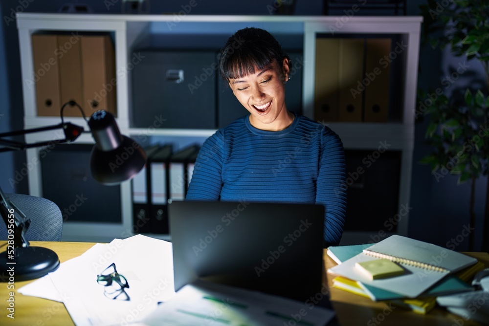 Young beautiful woman working at the office at night winking looking at the camera with sexy expression, cheerful and happy face. Young beautiful woman working at the office at night winking looking at the camera with sexy expression, cheerful and happy face.
