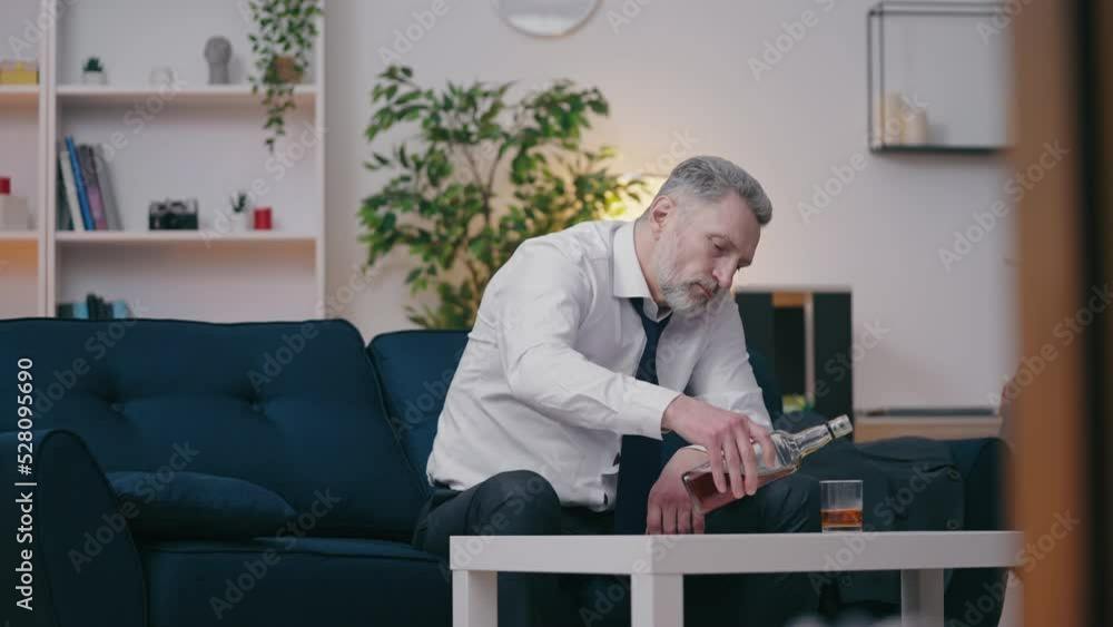 Depressed middle-aged man in suit pouring alcohol in glass, harmful addiction Depressed middle-aged man in suit pouring alcohol in glass, harmful addiction