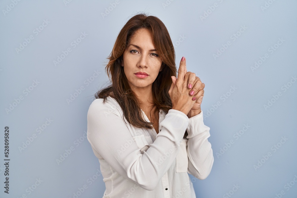 Hispanic woman standing over isolated background holding symbolic gun with hand gesture, playing killing shooting weapons, angry face Hispanic woman standing over isolated background holding symbolic gun with hand gesture, playing killing shooting weapons, angry face