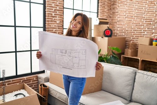 Young latin woman smiling confident holding house plan at hew home