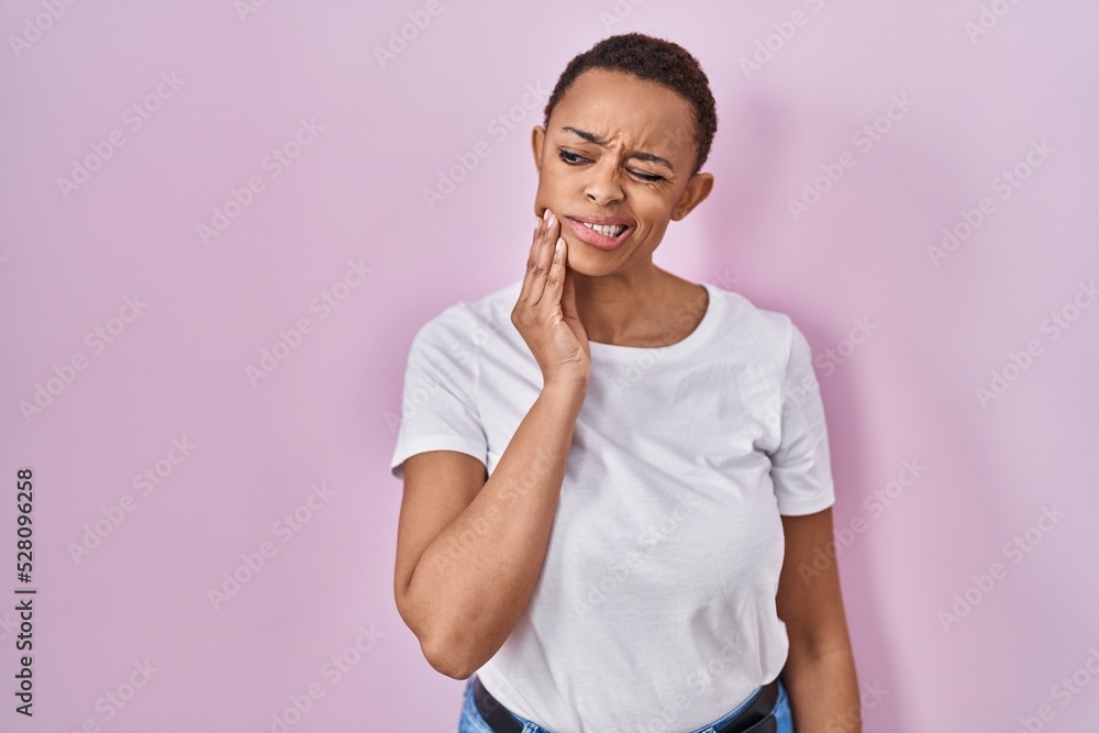 Beautiful african american woman standing over pink background touching mouth with hand with painful expression because of toothache or dental illness on teeth. dentist