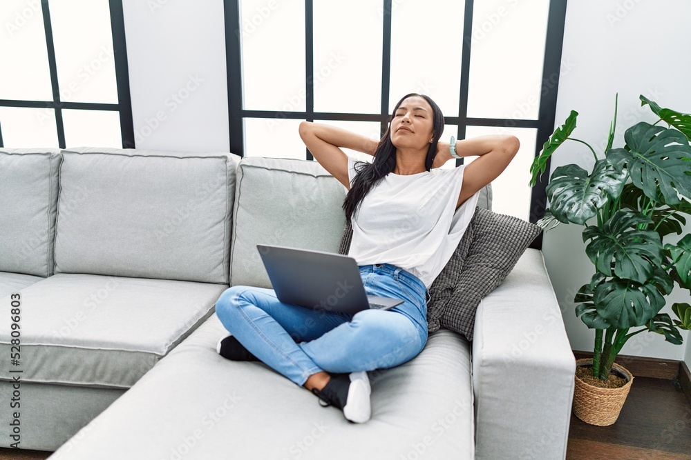 Young latin woman using laptop relaxed with hands on head at home Young latin woman using laptop relaxed with hands on head at home