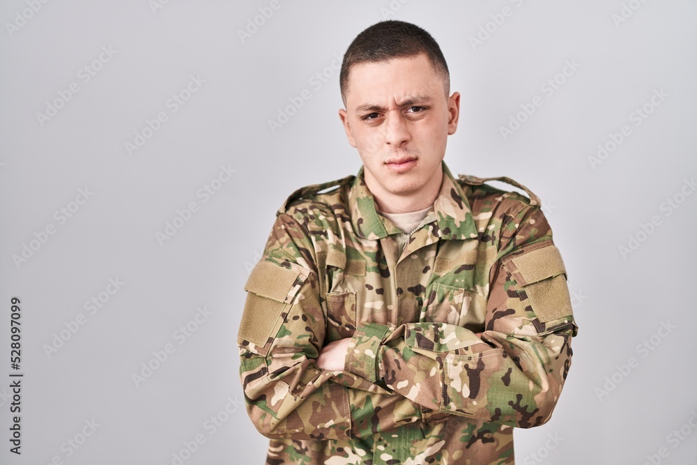 Young man wearing camouflage army uniform skeptic and nervous, disapproving expression on face with crossed arms. negative person.