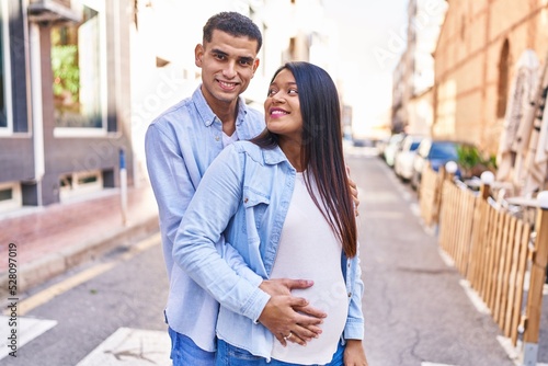 Young latin couple expecting baby hugging each other standing at street