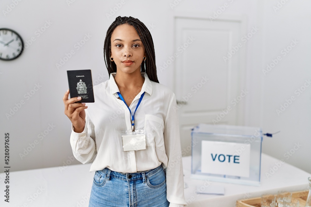 Young african american woman at political campaign election holding canada passport thinking attitude and sober expression looking self confident Young african american woman at political campaign election holding canada passport thinking attitude and sober expression looking self confident