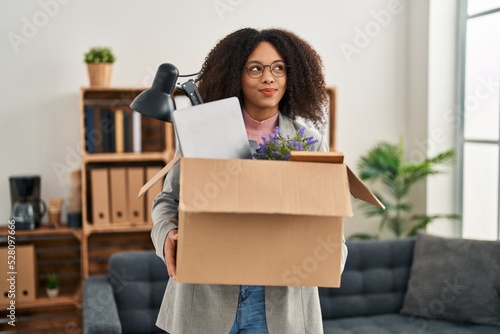 Young african american woman moving to a new office holding box with items smiling looking to the side and staring away thinking.