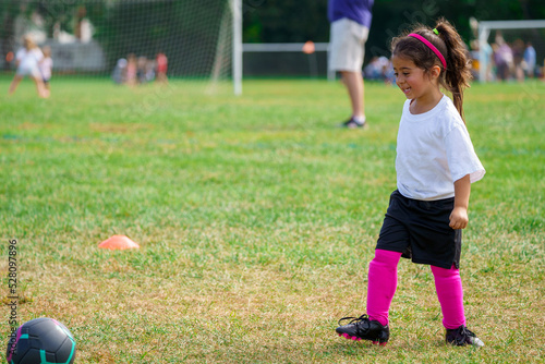 Adorable happy young girl playing peewee soccer on a green field during autumn league season. Toddler learning sports and discipline of team sports. Weekend family activity in typical suburban life