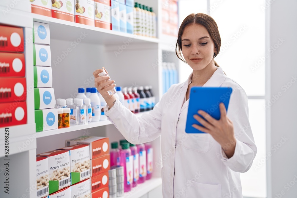 Young woman pharmacist using touchpad holding bottle at pharmacy