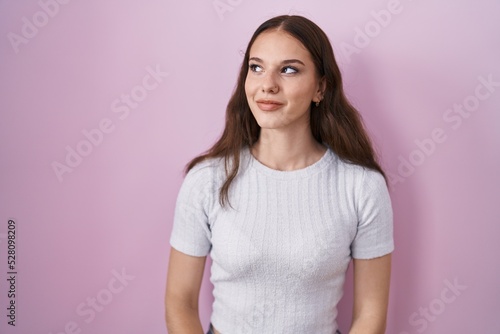 Young hispanic girl standing over pink background smiling looking to the side and staring away thinking.