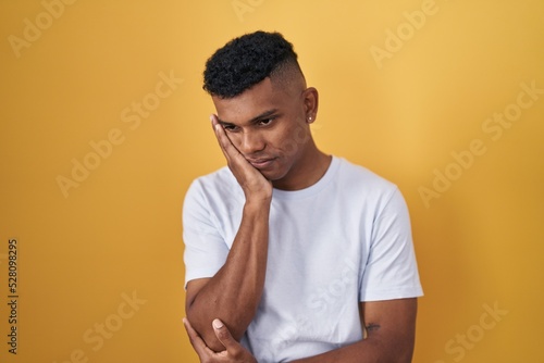 Young hispanic man standing over yellow background thinking looking tired and bored with depression problems with crossed arms. © Krakenimages.com