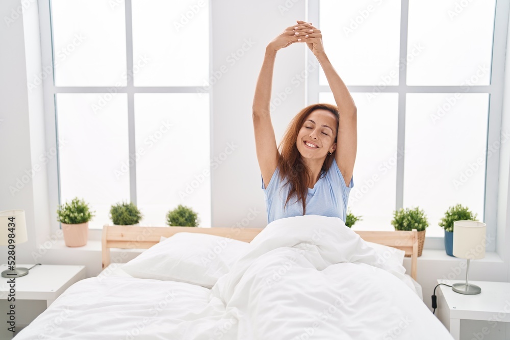 Young woman stretching arms sitting on bed at bedroom Young woman stretching arms sitting on bed at bedroom
