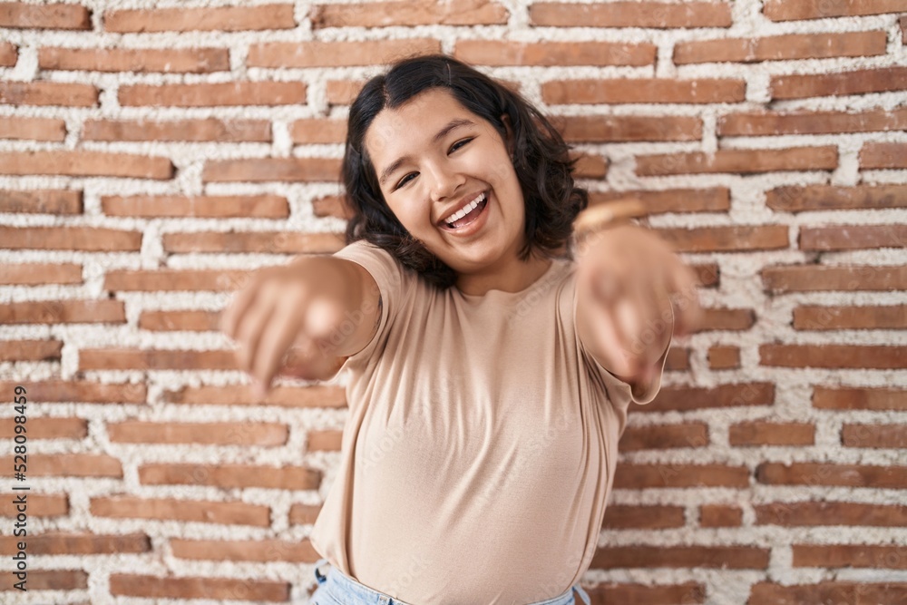 Young hispanic woman standing over bricks wall pointing to you and the camera with fingers, smiling positive and cheerful Young hispanic woman standing over bricks wall pointing to you and the camera with fingers, smiling positive and cheerful