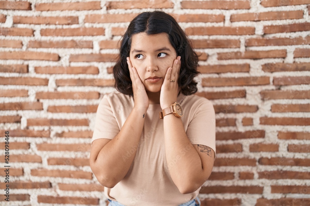 Young hispanic woman standing over bricks wall tired hands covering face, depression and sadness, upset and irritated for problem Young hispanic woman standing over bricks wall tired hands covering face, depression and sadness, upset and irritated for problem