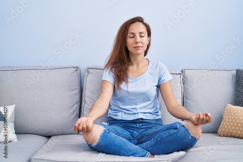 Young woman doing yoga exercise sitting on sofa at home