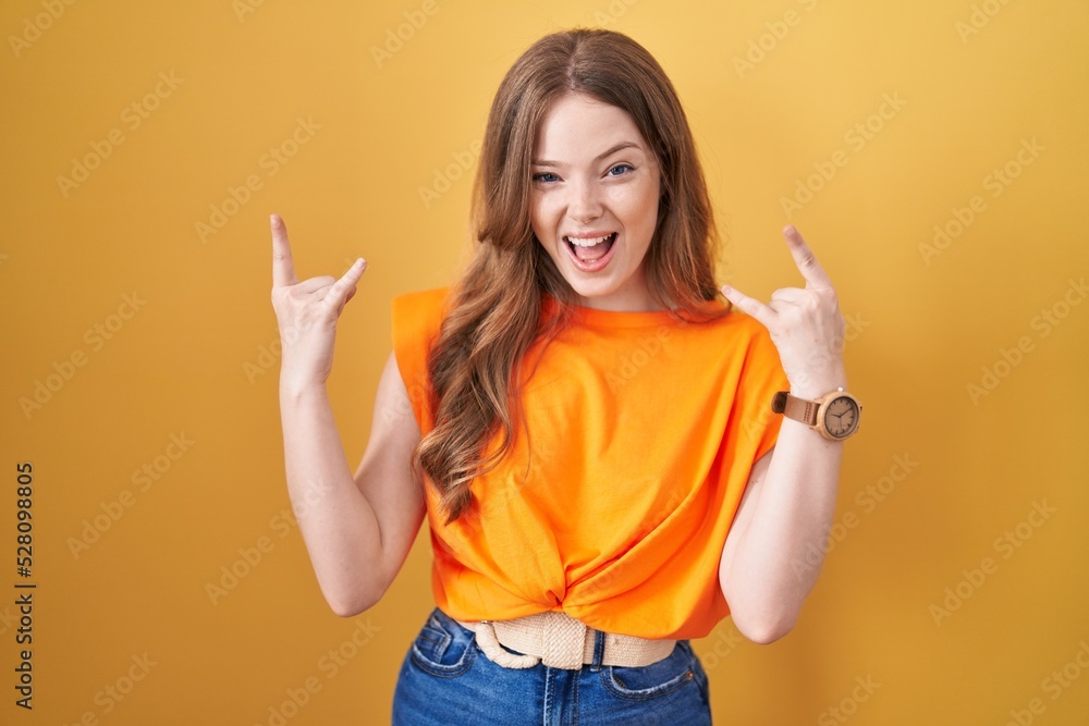 Caucasian woman standing over yellow background shouting with crazy expression doing rock symbol with hands up. music star. heavy music concept. Caucasian woman standing over yellow background shouting with crazy expression doing rock symbol with hands up. music star. heavy music concept.