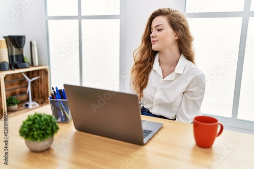Young caucasian woman working at the office using computer laptop looking to side, relax profile pose with natural face and confident smile. © Krakenimages.com