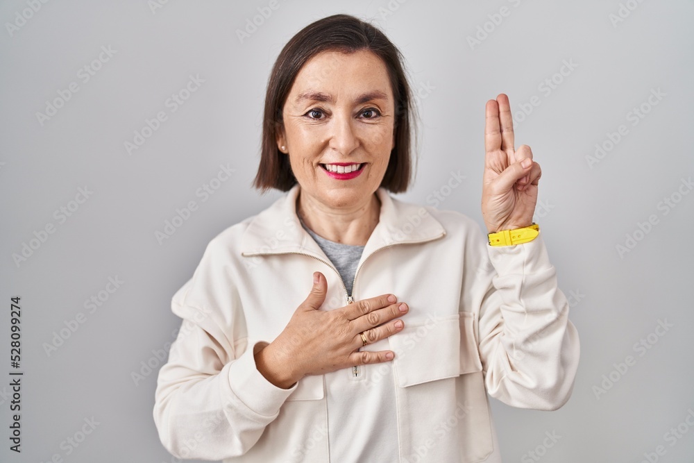 Middle age hispanic woman standing over isolated background smiling swearing with hand on chest and fingers up, making a loyalty promise oath Middle age hispanic woman standing over isolated background smiling swearing with hand on chest and fingers up, making a loyalty promise oath