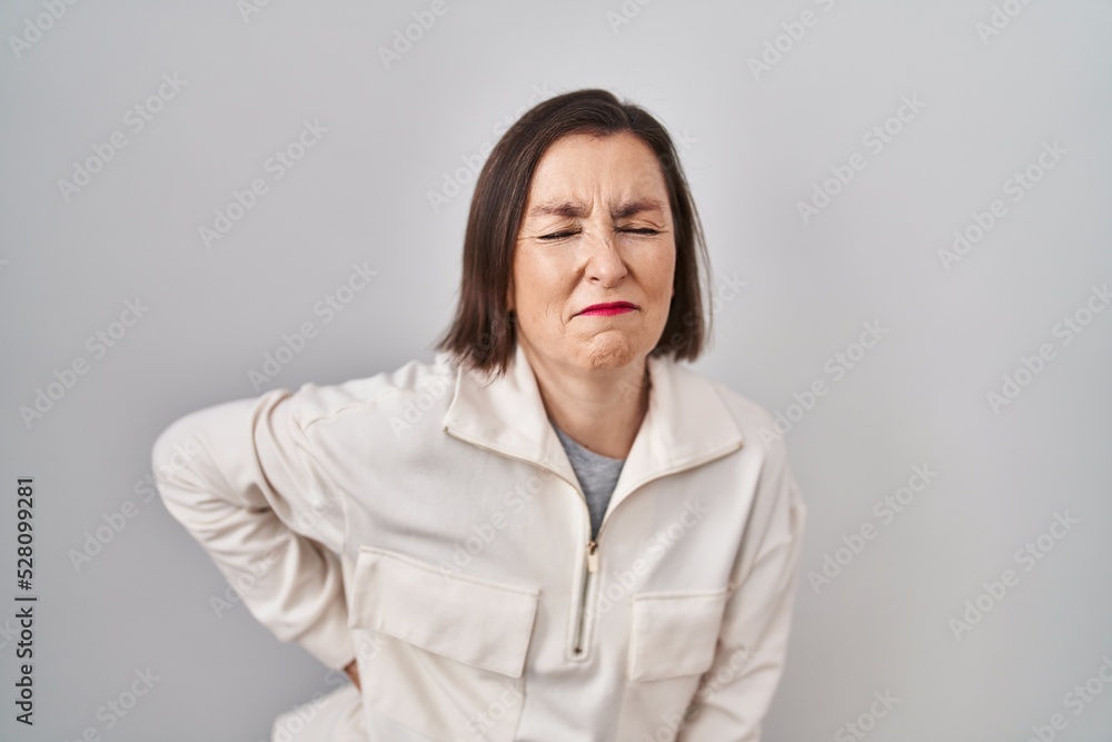 Middle age hispanic woman standing over isolated background suffering of backache, touching back with hand, muscular pain Middle age hispanic woman standing over isolated background suffering of backache, touching back with hand, muscular pain