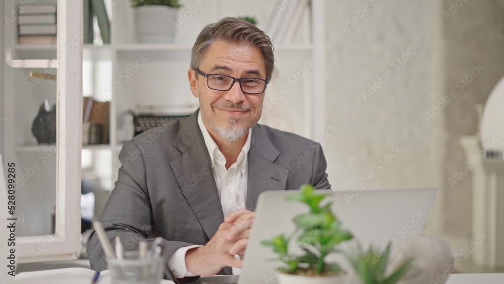 Businessman working with laptop computer in home office. Portrait of happy confident middle aged, mid adult, mature age man smiling. Entrepreneur sitting at desk, managing business online. Businessman working with laptop computer in home office. Portrait of happy confident middle aged, mid adult, mature age man smiling. Entrepreneur sitting at desk, managing business online.