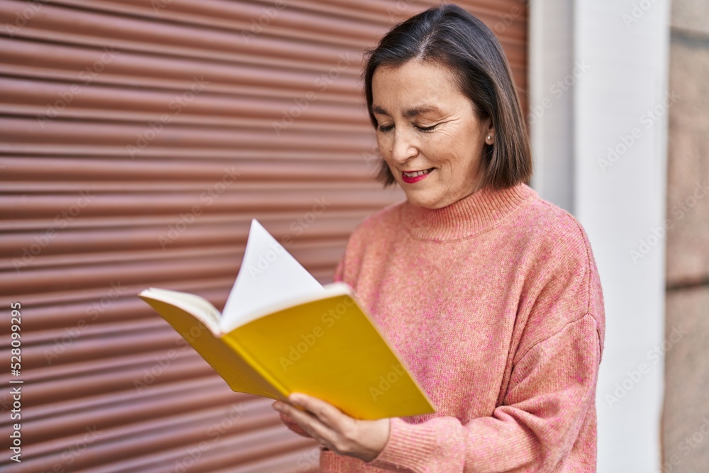 Middle age woman smiling confident reading book at street Middle age woman smiling confident reading book at street