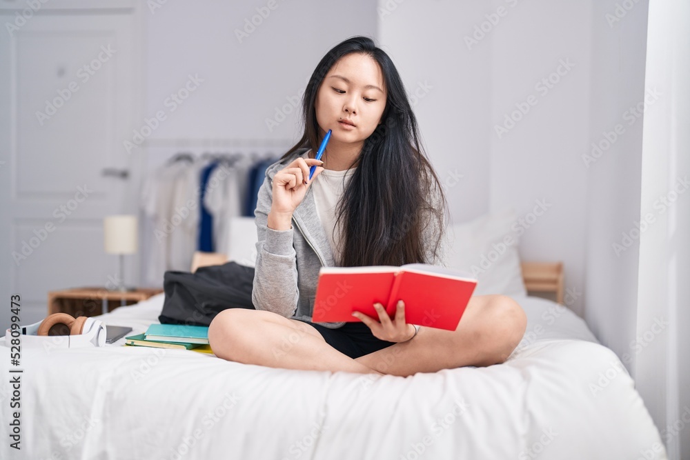 Young chinese woman writing on notebook with doubt expression at bedroom Young chinese woman writing on notebook with doubt expression at bedroom