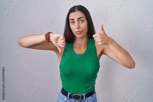 Young woman standing over isolated background doing thumbs up and down, disagreement and agreement expression. crazy conflict