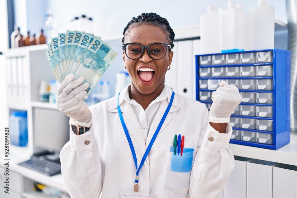 African woman with braids working at scientist laboratory holding money screaming proud, celebrating victory and success very excited with raised arm