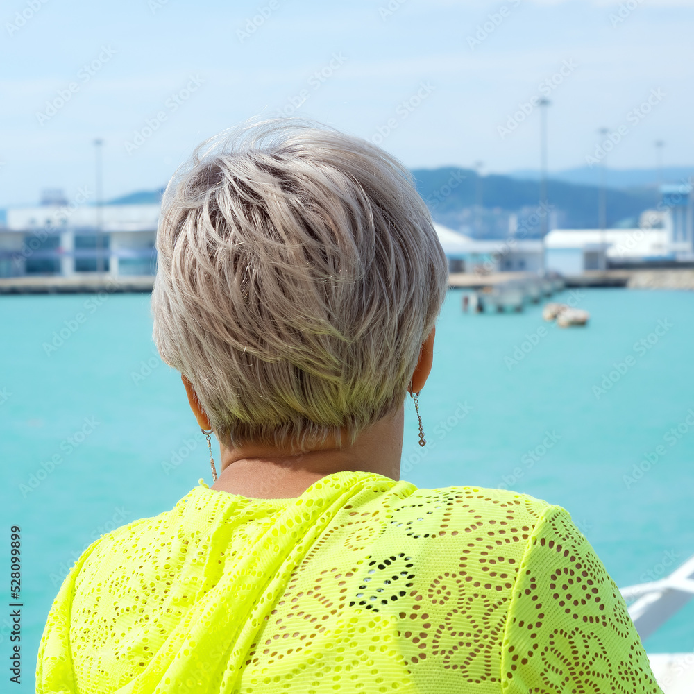 Fototapeta premium A blonde girl with a short hair looks at the sea. Pretty haircut